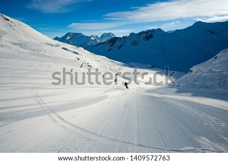 Panoramic landscape valley view with skiers going down a ski slope piste in winter alpine mountain resort