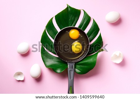 Creative layout of egg in pan over monstera leaf on pink background. Minimalistic food concept. Top view