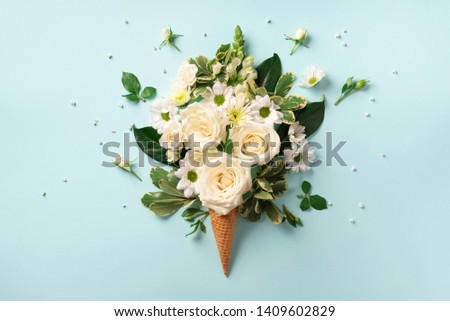 Summer minimal concept. Ice cream cone with white flowers and leaves on blue background. Flat lay. Top view. Creative layout.