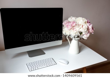 Spacious clean workspace. On the table is a computer and flowers peonies.