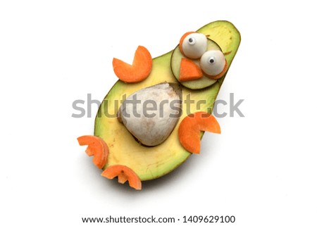 Food art creative concept. Funny penguin made of avocado, cucumber and carrots over white background.  Creative fun healthy food concept, an avocado cut in half with  funny googly eyes.