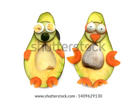 Food art creative concept. Funny couple penguins made of avocado, cucumber and carrots over white background.  Creative fun healthy food concept, an avocado cut in half with  funny googly eyes.
