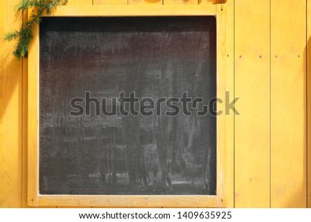 Empty space concept for advertising, mockup. Front view of a blank blackboard for text with Christmas tree branches and wooden surface in background.