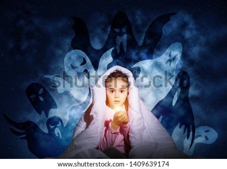 Scared girl with flashlight hiding under blanket from imaginary ghosts. Kid sitting in bed on night sky background. Covered child in pajamas not sleep at night. Mysterious phantoms in darkness.