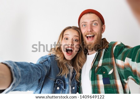 Excited young stylish couple standing isolated over white background, taking a selfie