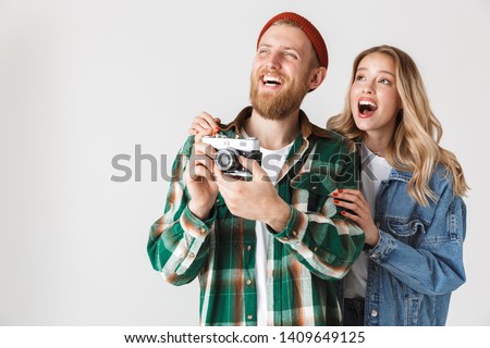 Excited young stylish couple standing isolated over white background, holding photo camerato make pictures