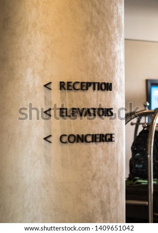 A sign in a luxury hotel showing the directions for the reception, elevator and concierge service.