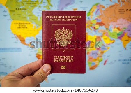 Hand holding the passport of Russia against the colorful world map atlas. Russian passport concept, Russian tourists travel concept.