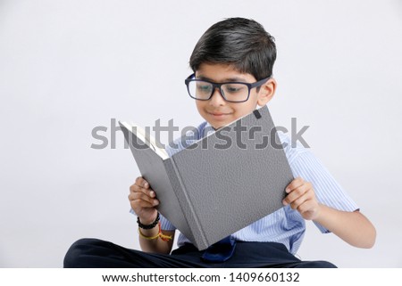 Cute little Indian/Asian school boy with spectacles reading book over white background