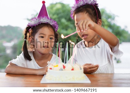 Two cute asian child girls lighting candle on birthday cake together in birthday party