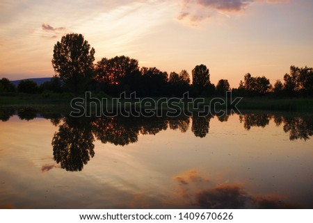 Beautiful sunset of a calm lake with refletions of trees and clouds
