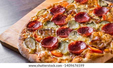 Pepperoni Pizza with Mozzarella cheese, salami, bacon, Tomato sauce, pepper, Spices and pickled cucumbers. Italian pizza on wooden table background