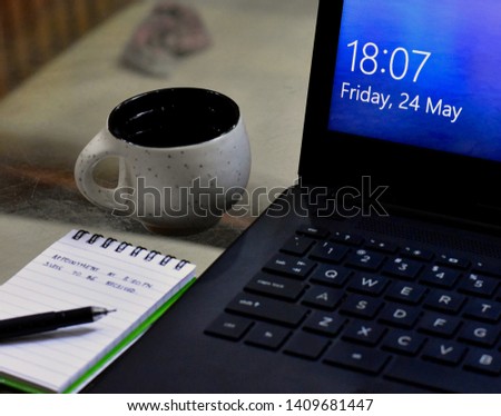 Picture of a cup of coffee in focus near a laptop and notepad.