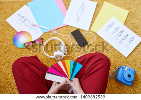 View of female designer with color swatches sitting on the floor while working over new fashion collection at home