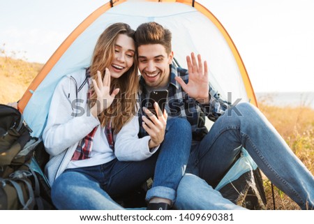 Photo of happy young loving couple outside in free alternative vacation camping talking by mobile phone waving.