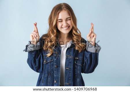 Image of a beautiful young pretty woman posing isolated over blue wall background make hopeful please gesture fingers crossed.