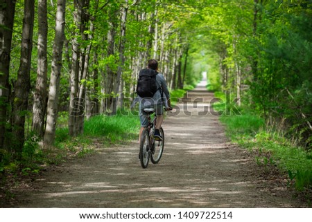 Young man biking cycling through the park alley green tunnel made of tree brunches. Summer  spring scene. Recreational sport and cycling concept. Selective focus. Caledon trailway path, Ontario.