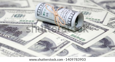 US dollars rolled up and tightened with band lies on a lot of american banknotes with blurred background