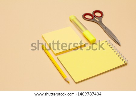 Scissors, pencil, notebook, note-paper and yellow felt-tip pen on beige background. Back to school concept. School supplies. Pastel colors