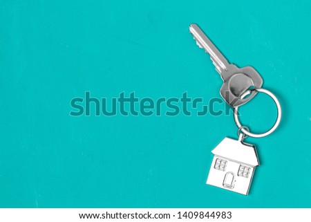 Silver house keyring with key on turquoise background with copy space