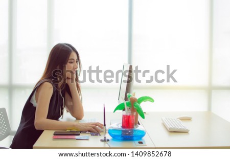 An asian beautiful woman is sitting in front of her computer and searching on the internet to plan her summer trip