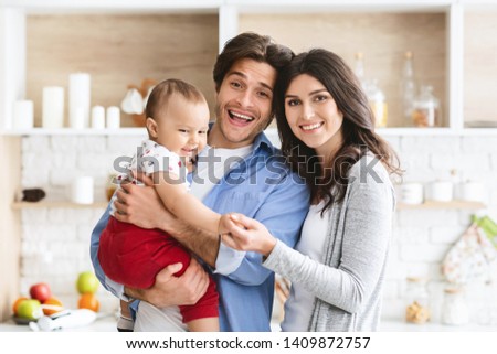 Portrait of happy millennial family. Cheerful mother, father and baby at kitchen interior