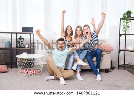 Group of young people watching tv. Active youth at home cheering on the team. Cheerful friends indoors having fun together.