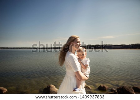 Happy mother huges baby near the sea. Mother holds child in her arms, baby hugging mom