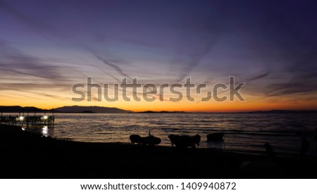 Dramatic sunset landscape at Urla, Izmir, Turkey. Beautiful blazing sunset over bright blue sea, pier, jet trails, orange sky above it with awesome golden rays of sun light reflection on calm waves.