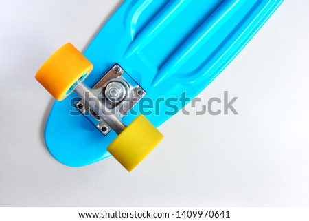 Detail of blue plastic mini cruiser penny board or skate board with yellow and orange wheels and metal attachment on light grey background with copy space. Back view in soft light   