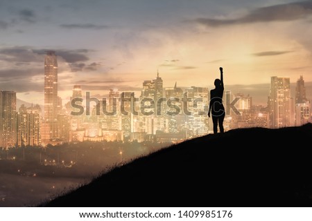 Strong woman with fist in the air standing on top a mountain overlooking the city. Triumph, victory and feeling determined. Royalty-Free Stock Photo #1409985176