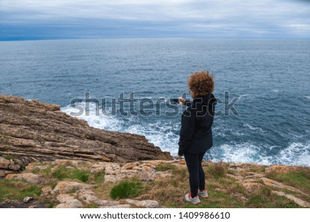 Mature redhead woman taking a picture with the cell phone, on her back, dressed to play sports in black. With the coast and the sea in the background, a cloudy spring afternoon