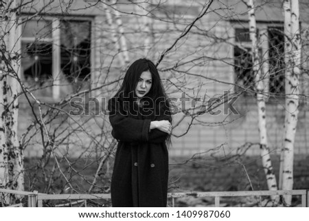 Young woman in black clothes at the background of an abandoned house