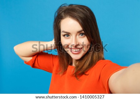 Close up photo of young woman in red orange clothes looking camera posing doing selfie shot isolated over trendy blue background, studio portrait. People lifestyle fashion concept. Mock up copy space