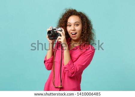 Excited african girl in casual clothes taking picture on retro vintage photo camera isolated on blue turquoise wall background in studio. People sincere emotions lifestyle concept. Mock up copy space