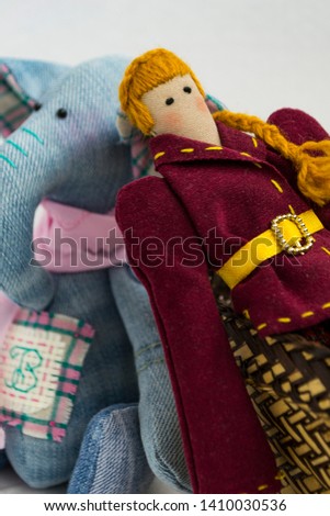 A female tilde doll in colorful clothes is sitting in a wicker basket on a white background. Registration of holidays. Interior fairy doll handmade. Art and creativity. Blurred background.