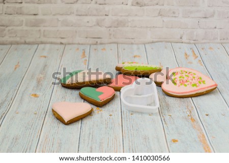 Pink and colored gingerbread and honey cakes and heart-shaped cookies lie in a messy pile on a light wooden background. Nearby are white molds for baking. Place for text. The concept of love, mother's