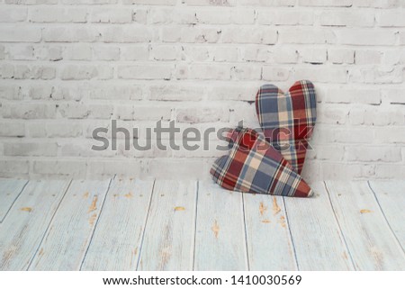 Two handmade hearts from checkered fabric stand on a light brick background, and on a light background of a wooden table with copy space. The concept of love, congratulation, manual labor needlewoman.