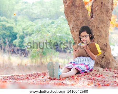 Cute little girl with glasses reading a book under big flower tree