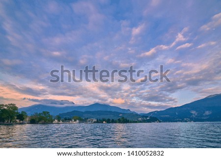 View of the beautiful Riva del Garda town at sunset with a red sky, Lake Garda surrounded by mountains in the summer, Italy