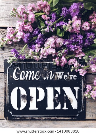 Come in we’re open sign with flowers on a rustic wooden background