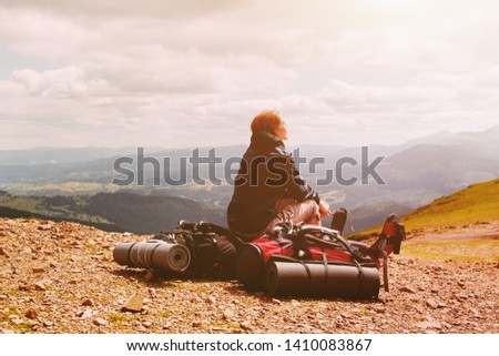 Young blonde woman tourist resting on a hiking backpack in the mountains
