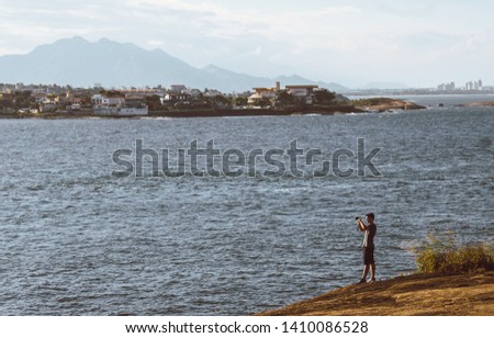 man take a photo of sea, montain in background blue sky sea