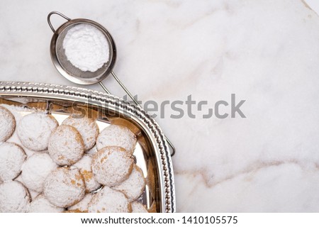 Kahk cookies served on a silver big plate sprinkled with sugar on top (Kahk is a traditional cookies in the arab world, served in Eid el fitr, a feast after Ramadan)  on a white marble background
