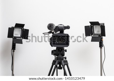 video camera on the tripod and spotlight harogen lamp isolated on white background, in concept of movie making equipment, TV production.