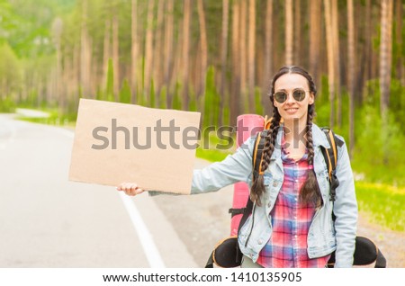 Young woman travels hitchhiking with a cardboard sign in her hands. Space for text
