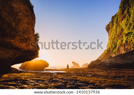 Slim woman posing near ocean with rocks and sunset. Woman in bikini at ocean coast
