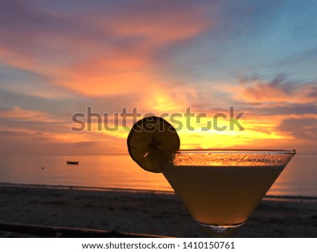 Cocktail glass with a slice of lemon on the background of the sea and sunset.