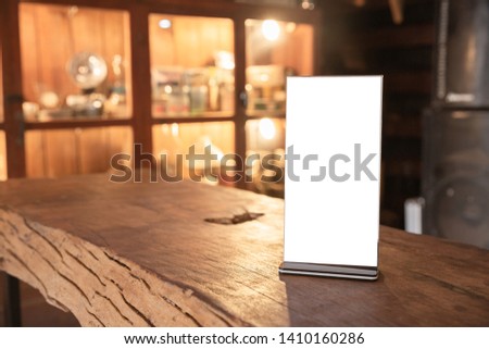Mock up Menu frame in Bar restaurant, Stand for booklets with white sheets of paper acrylic tent card on wooden table on cafeteria blurred background. 