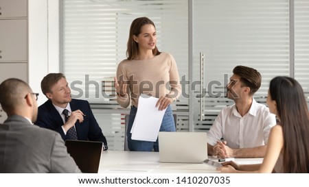 Confident female manager presenting financial report speak at team meeting talk to employees group, business woman company executive leader hold papers explain new business plan at corporate briefing Royalty-Free Stock Photo #1410207035